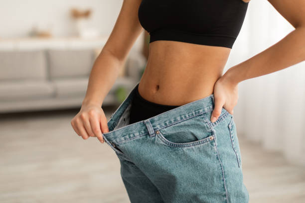 Woman holding out the waistband of loose jeans to show weight loss